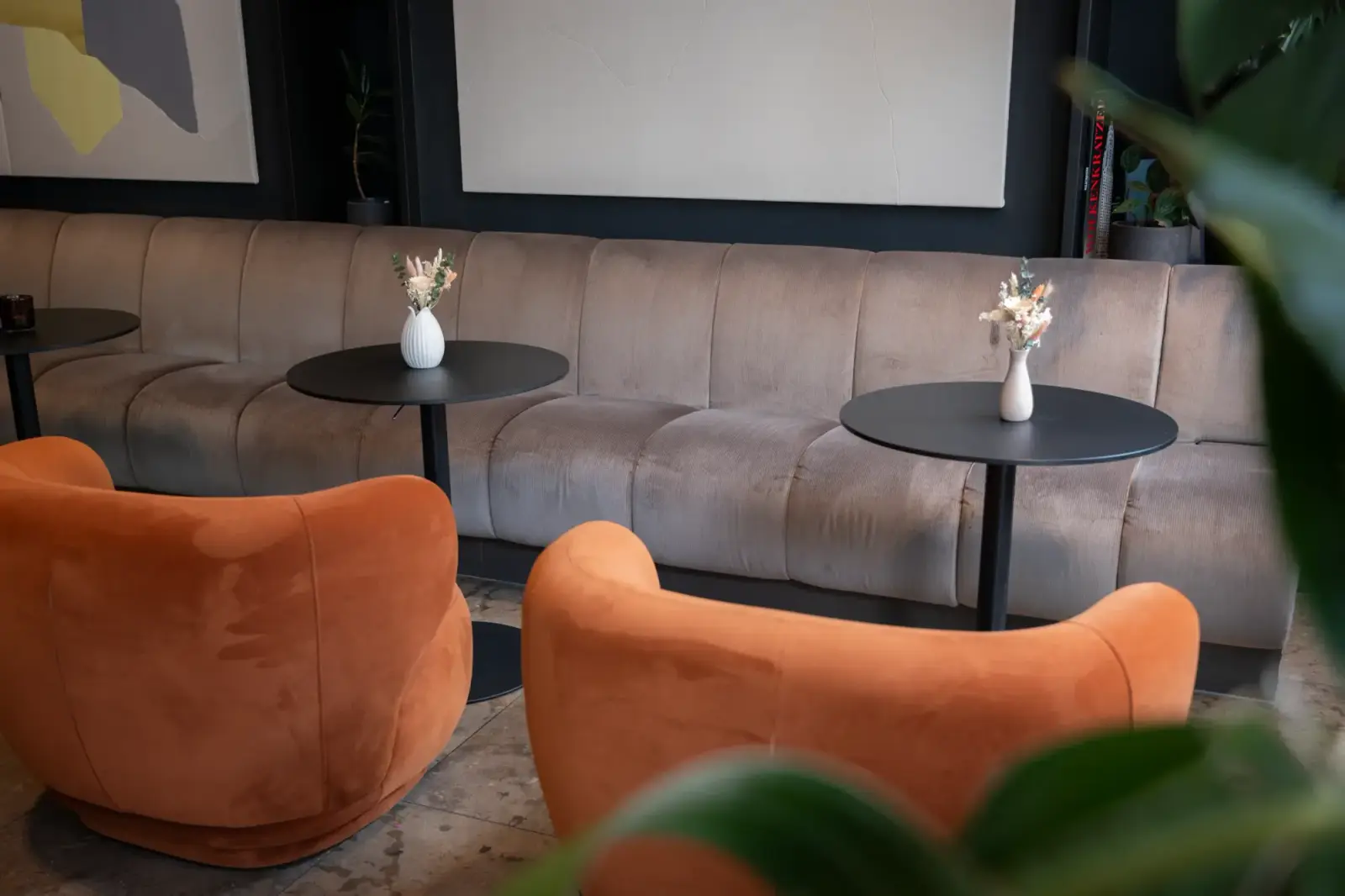 Lounge mit orangen Sesseln, Sofa und kleinen Vasen mit Trockenblumen auf den Tischen