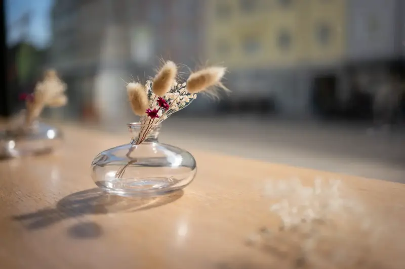 Kleine Glasvase mit Trockenblumen auf einem Holztisch, im Hintergrund die Straße