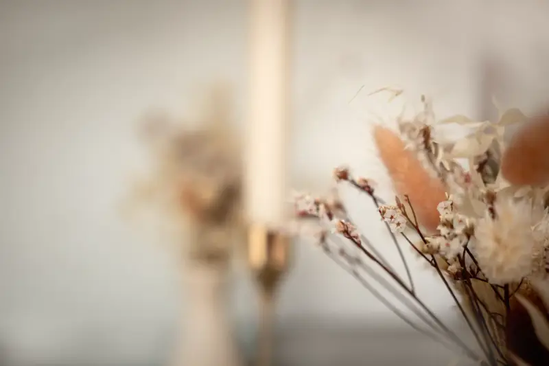 Trockenblumen in warmen Tönen neben einer Kerze