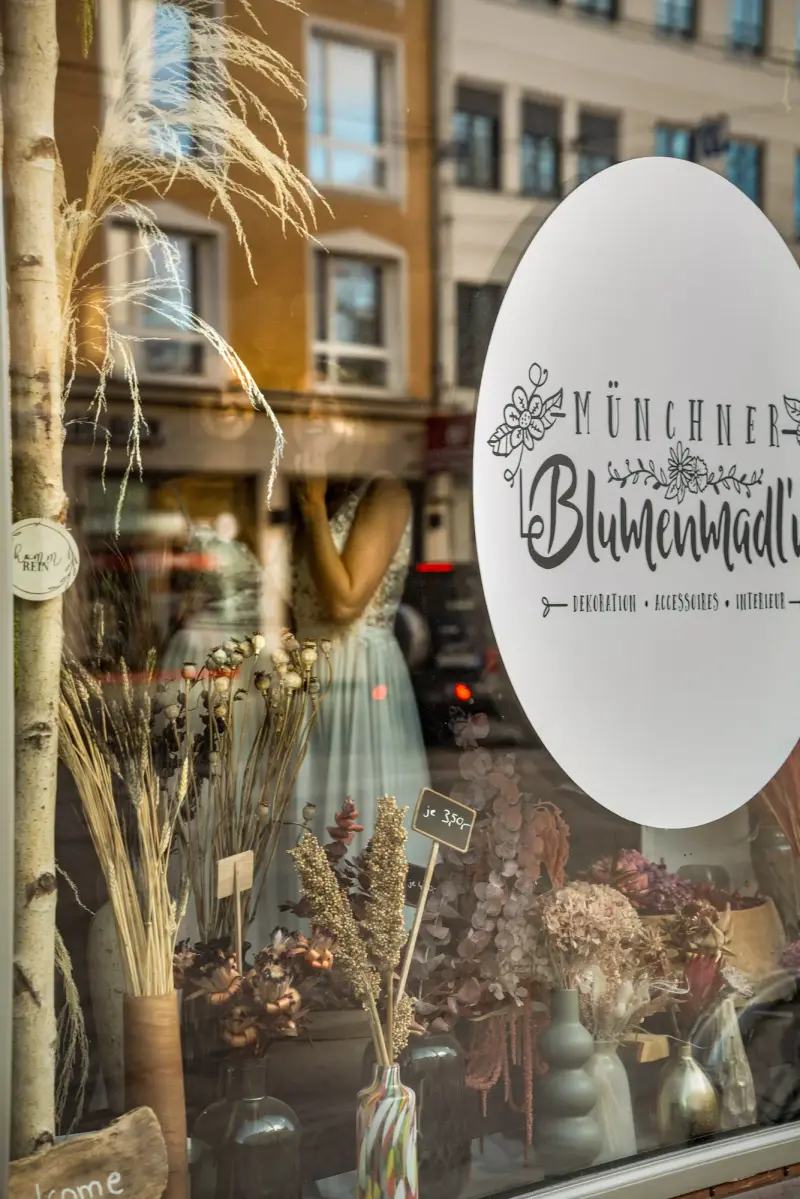 Schaufenster der Münchner Blumenmadl'n mit Logo und Trockenblumen, dahinter Häuser in Giesing